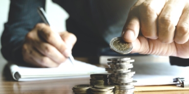 business man holding a coin to put on the top the pile of coins and writing calculate his saving money.