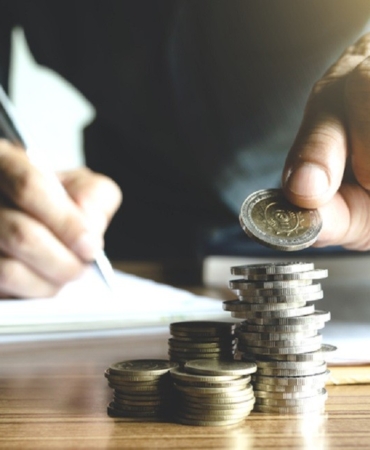 business man holding a coin to put on the top the pile of coins and writing calculate his saving money.