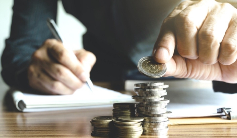 business man holding a coin to put on the top the pile of coins and writing calculate his saving money.